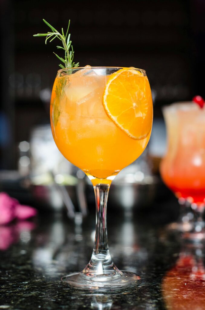 Refreshing orange cocktail with ice, garnished with rosemary and orange slice. Perfect for summer parties.